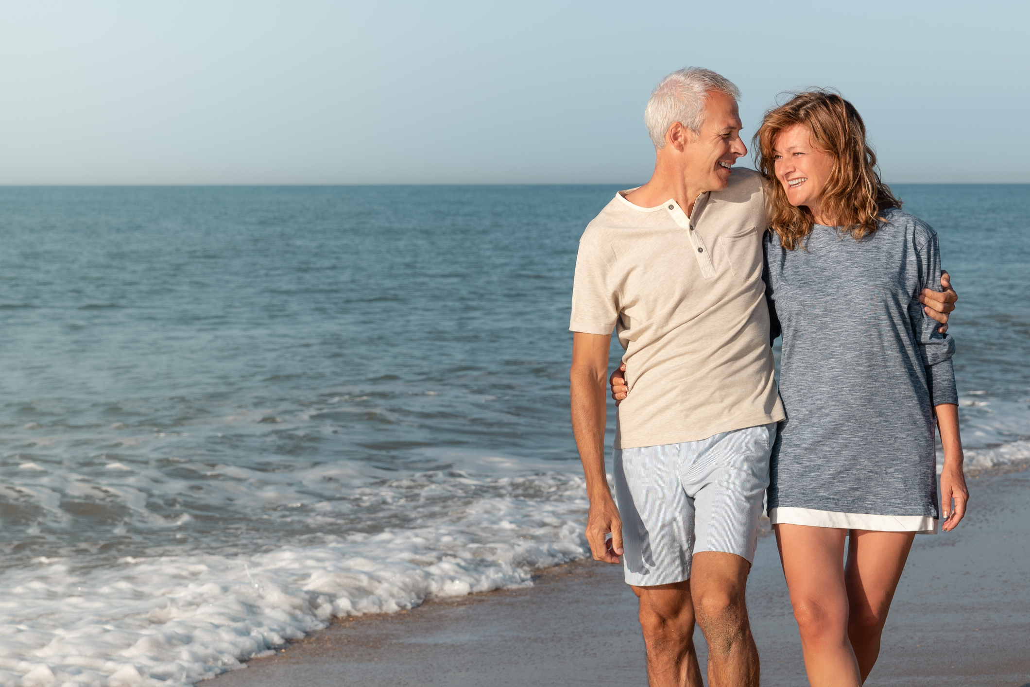 Mature man and woman hugging while laughing while walking along the seashore on a summer day