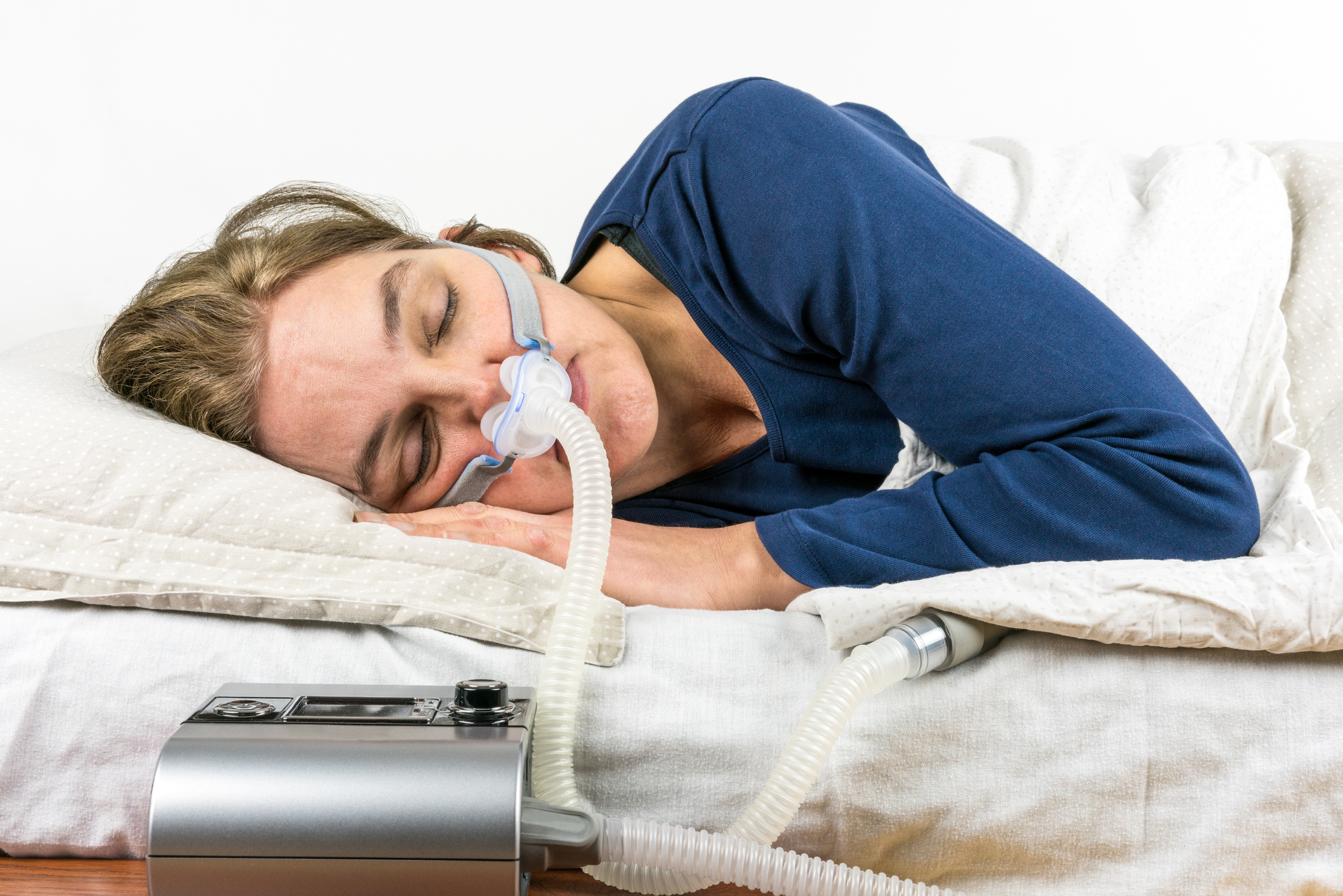Woman sleeping on her side with CPAP machine in the foreground, sleep apnea treatment.